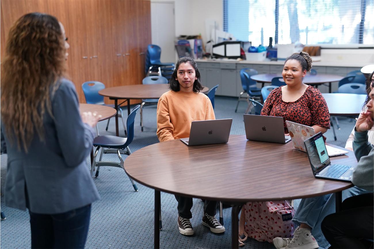 Students sitting at a table listening to a teacher