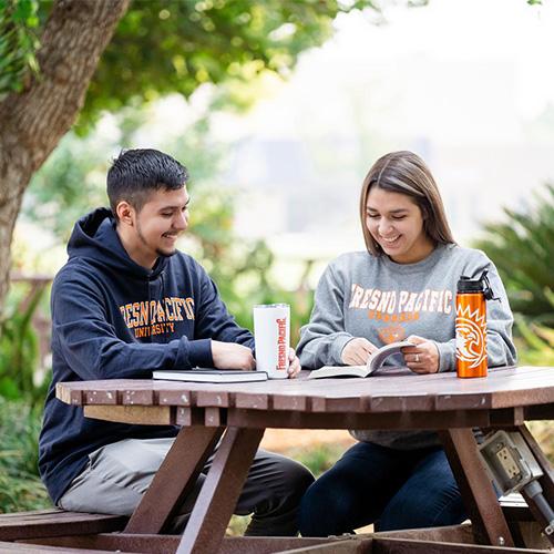 Photo of two students sitting at a table outside