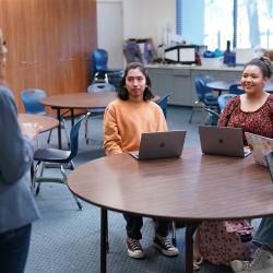 Students sitting at a table listening to a teacher